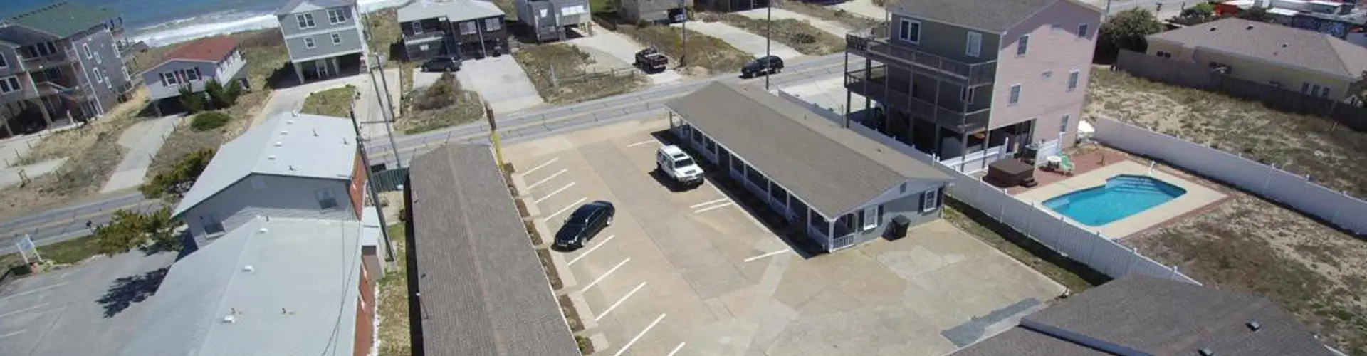Aerial view of Driftin Sands Motel and its parking lot, with the Kill Devil Hills oceanfront neighbourhood beyond