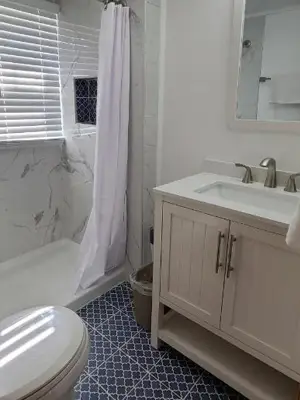 A white bathroom with a tub-and-shower combination, a single vanity and a mosaic-tile floor