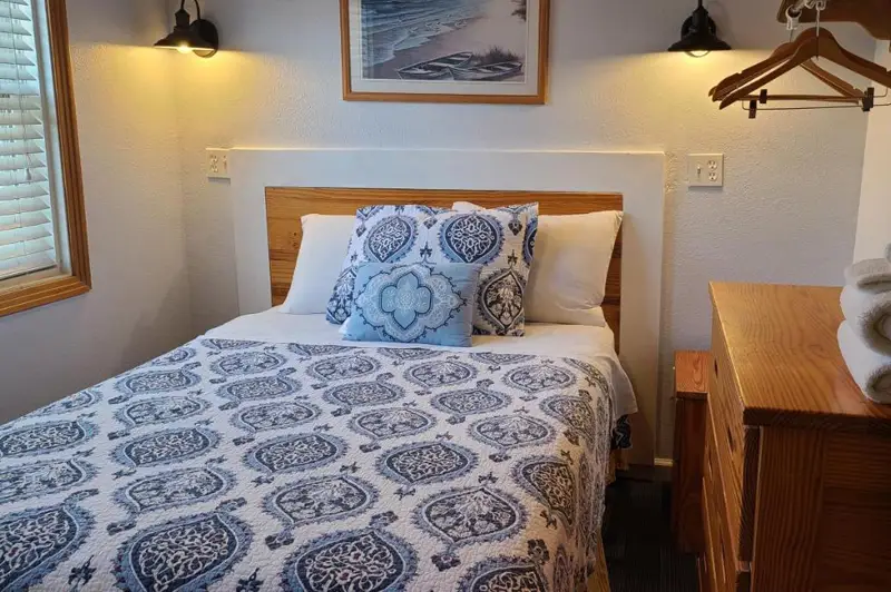 A bed with a blue medallion print and a lamp on the nightstand, beneath a framed print