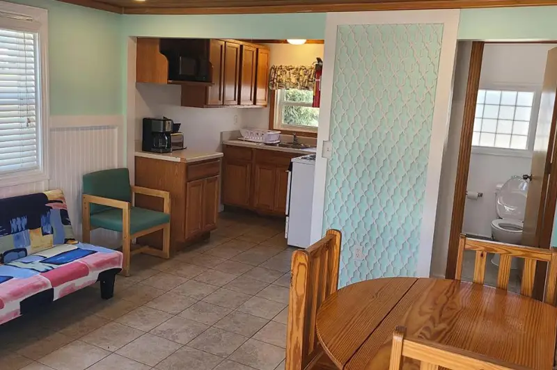 A kitchenette with wood cabinets, a coffee maker and a dining table, opening onto a bedroom