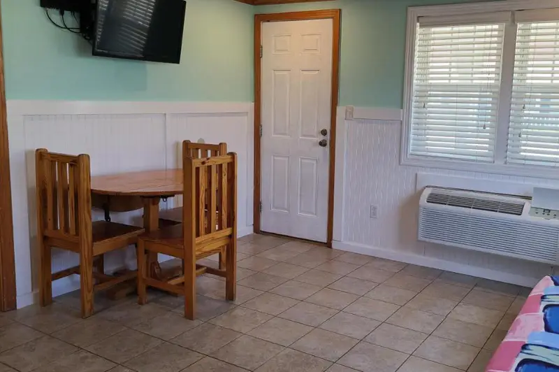 A small dining table and two chairs beside the entry door and a wall-mounted air conditioner