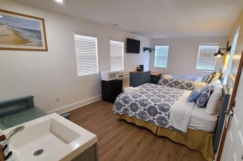 A guest room with two beds in a blue medallion print, a wall-mounted TV and windows with white blinds