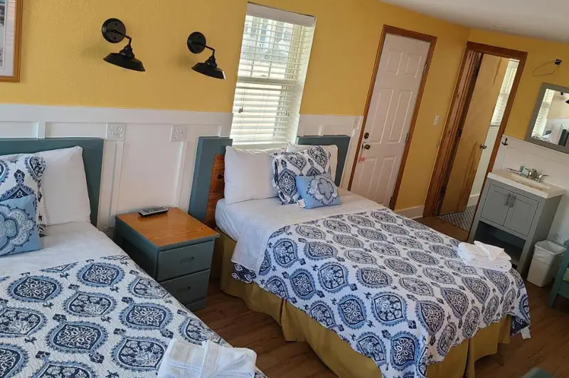 A guest room with two beds in a blue medallion print, wainscoted walls and wall-mounted reading lights