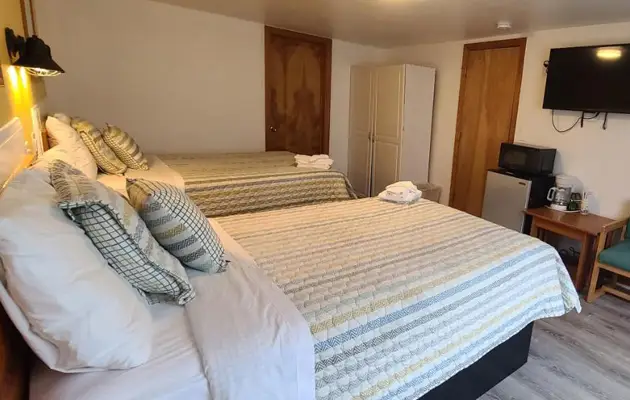 A guest room with two queen beds in striped bedding, a wall-mounted TV, a small table and a microwave stand